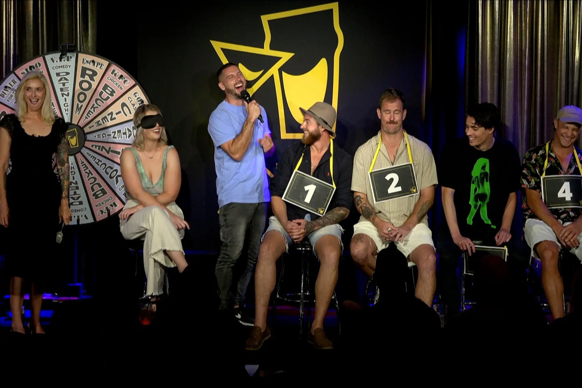 blind date comedy game show for singles to meet up. Contestants on stage laughing having a good time.